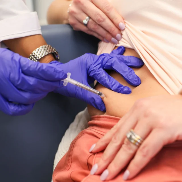 A person receives an injection in the abdomen from a healthcare professional wearing blue gloves.