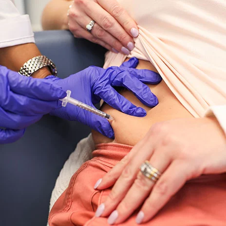 A healthcare professional wearing gloves administers an injection into a patient's abdomen.