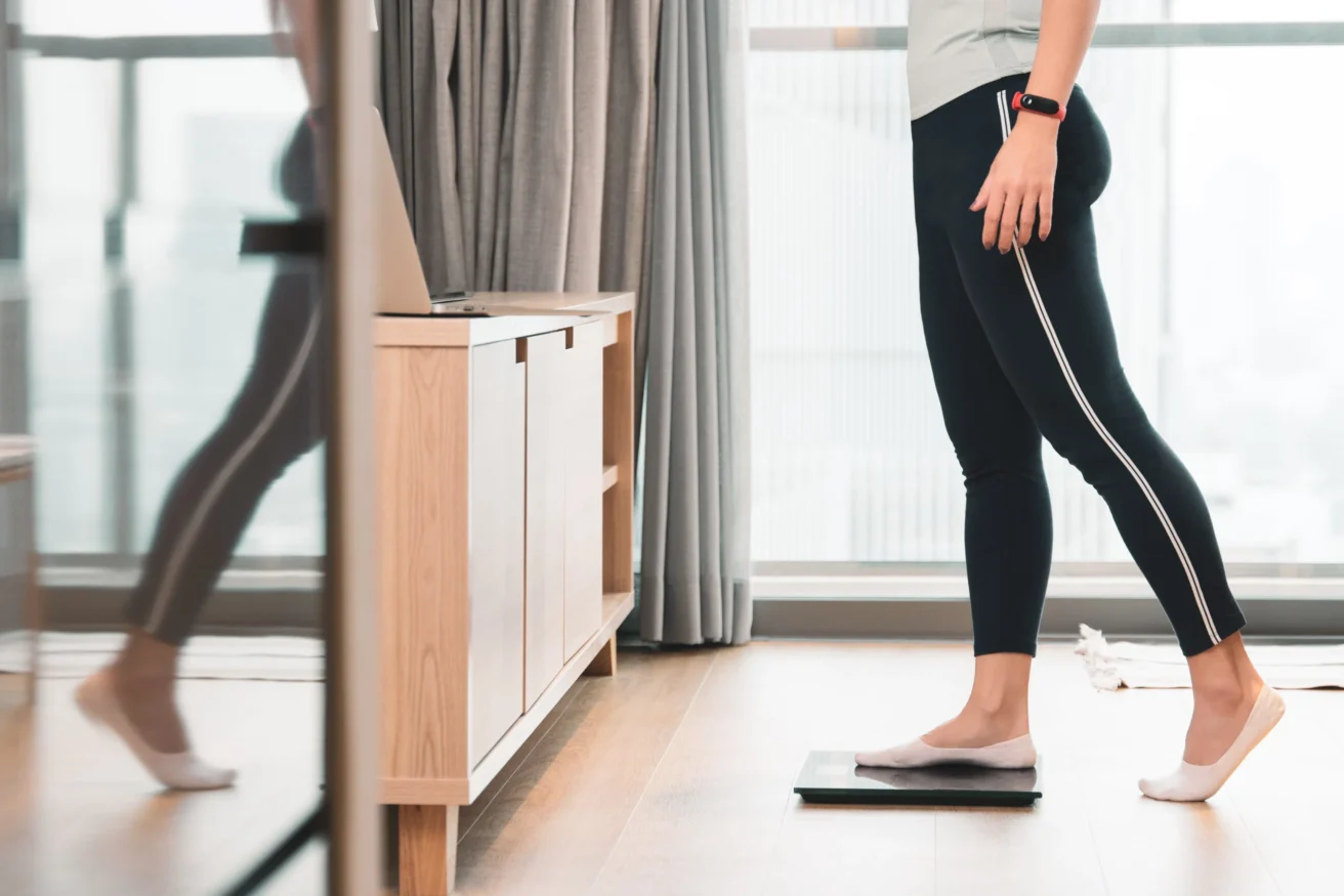 Person standing on a digital scale in a modern room with wooden flooring and furniture.