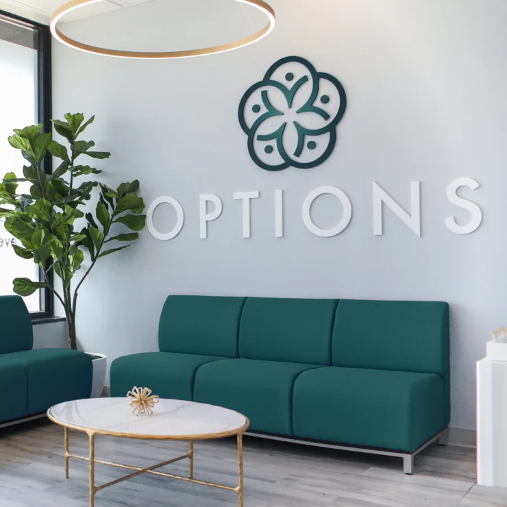 A modern waiting room with teal couches, a marble coffee table, a large plant, and a wall sign that says "OPTIONS" featuring a decorative logo above it.