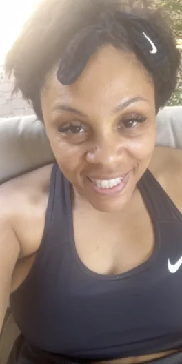 A woman in a black Nike sports bra and headband smiles at the camera while sitting outdoors.