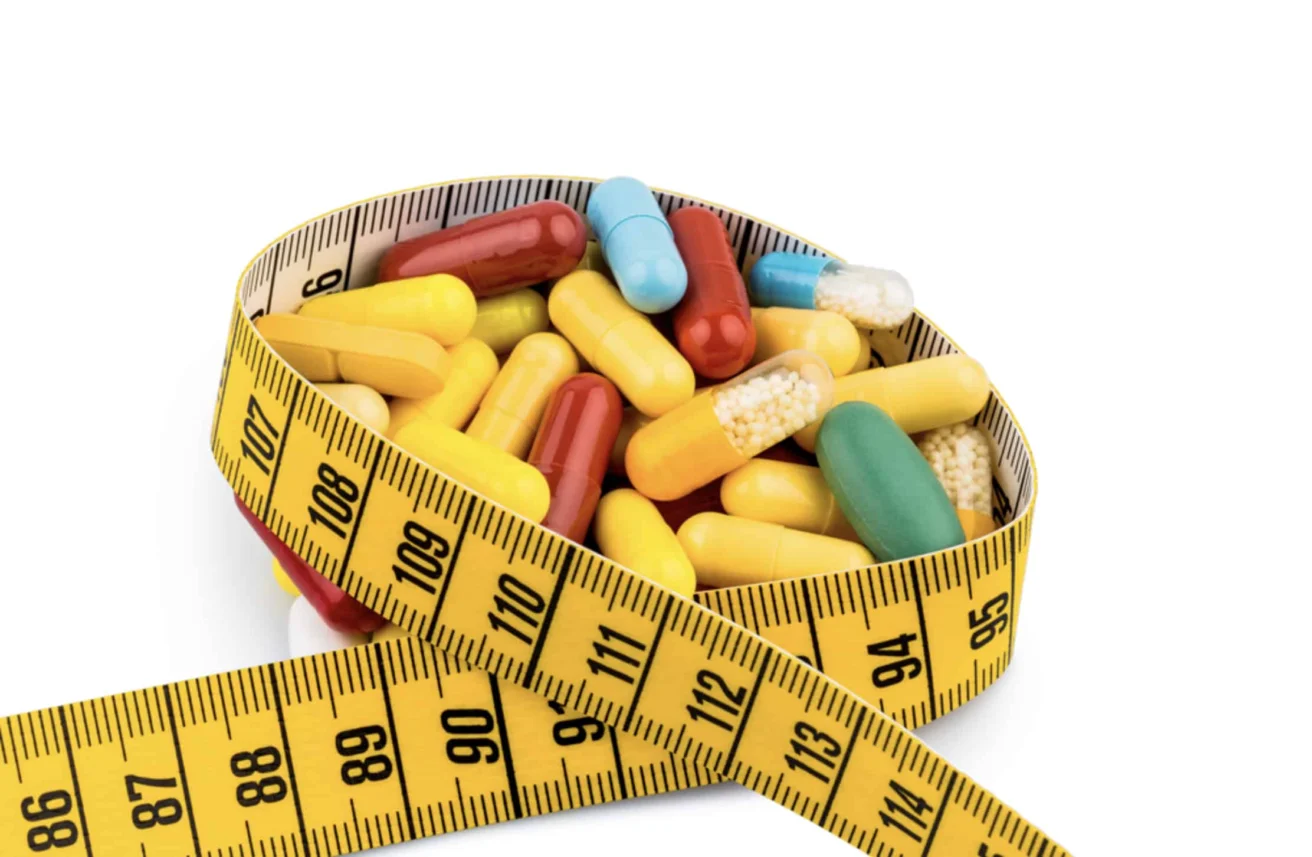 Various colorful capsules and pills are contained within a coiled yellow measuring tape against a white background.