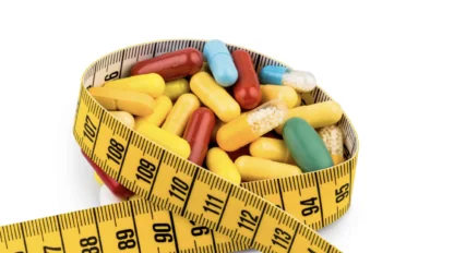 Various colorful capsules and pills are contained within a coiled yellow measuring tape against a white background.