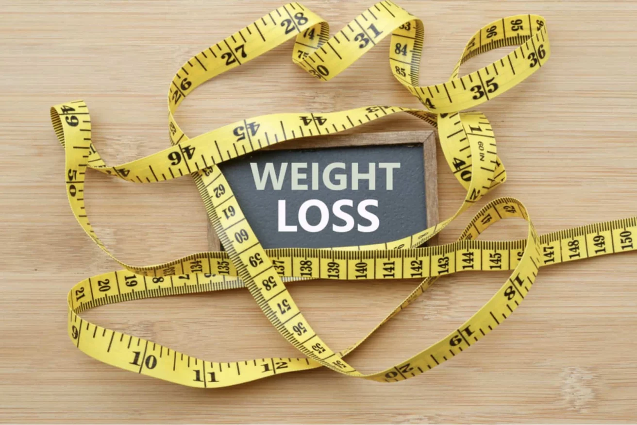 A chalkboard with the words "WEIGHT LOSS" is surrounded by yellow measuring tapes on a wooden surface.