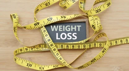 A chalkboard with the words "WEIGHT LOSS" is surrounded by yellow measuring tapes on a wooden surface.