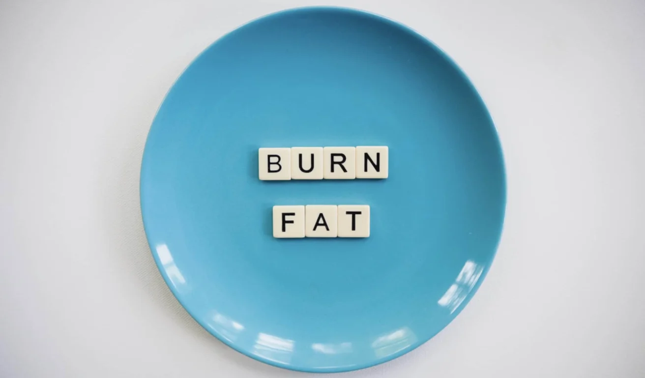 A blue plate with letter tiles spelling "BURN FAT" arranged in the center, placed on a white surface.