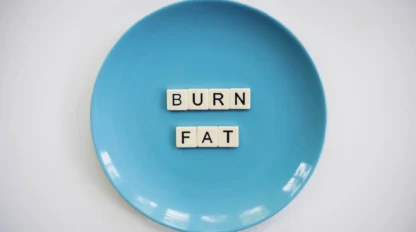 A blue plate with letter tiles spelling "BURN FAT" arranged in the center, placed on a white surface.
