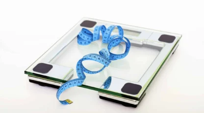 A glass digital bathroom scale with a blue measuring tape placed loosely on top, set against a white background.