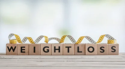 Wooden blocks spell "WEIGHT LOSS" on a wooden surface, with a yellow and white measuring tape coiled behind them.