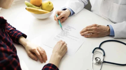 A doctor and patient review a medical form at a desk with a stethoscope and a bowl of fruit.