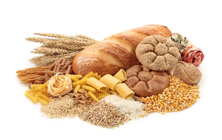 Assorted breads, pasta, grains, and wheat stalks arranged on a white background.
