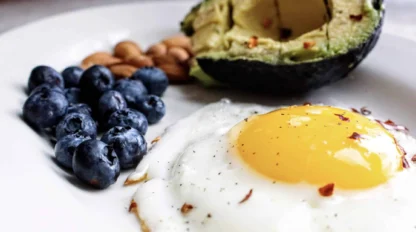 A plate with a sunny-side-up egg, half an avocado, a handful of almonds, and a small pile of blueberries.