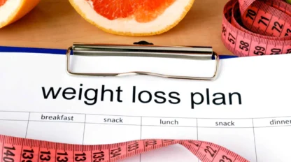 A clipboard with a weight loss plan chart, a pen, a pink measuring tape, and grapefruit slices on a wooden surface.