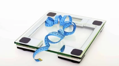 A digital glass bathroom scale with a blue measuring tape coiled on top, set against a plain white background.