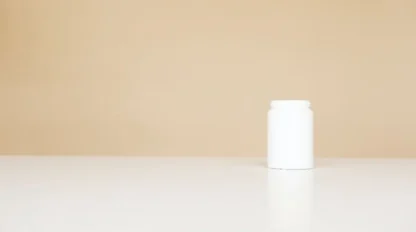 A small, plain white plastic jar with a lid sits on a white surface against a beige background. The container is centered to the right side of the image, and the scene is minimalistic.