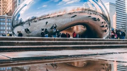 Cloud Gate sculpture in Chicago’s Millennium Park reflects the city skyline and people, with its image mirrored in a pool of water in the foreground.