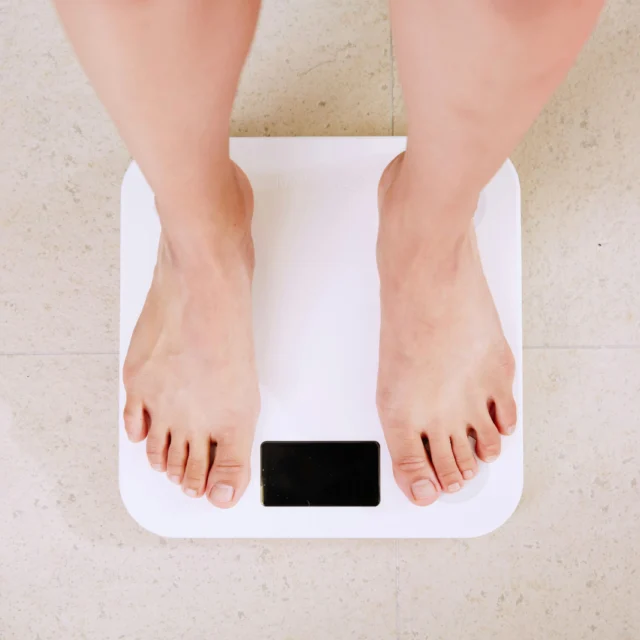 Person standing on a white digital scale on a tiled floor.