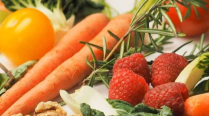 Assorted fresh vegetables, raspberries, walnuts, and rosemary arranged on a white surface.