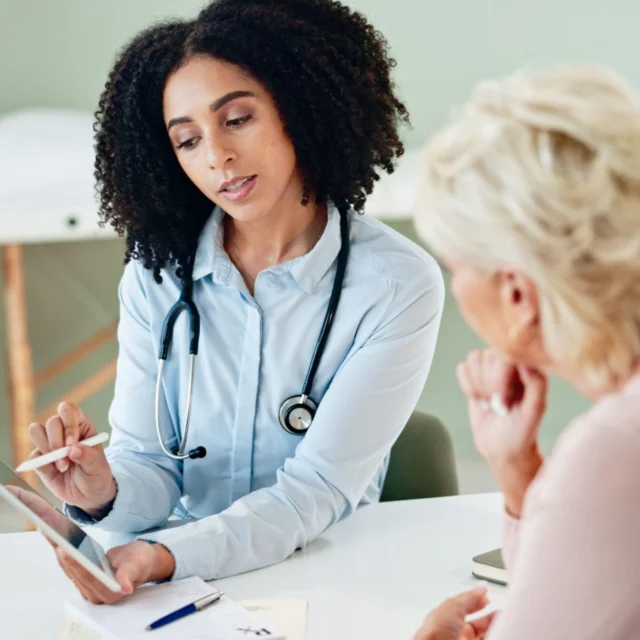 Doctor showing information on a tablet to a seated woman in an office setting.