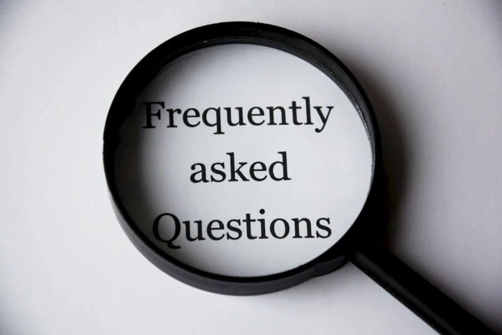 A magnifying glass focuses on the words "Frequently asked Questions" printed on white paper.