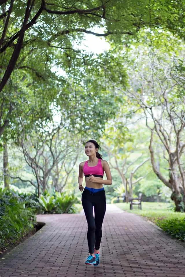 Woman jogging on a brick pathway in a park surrounded by green trees and plants.