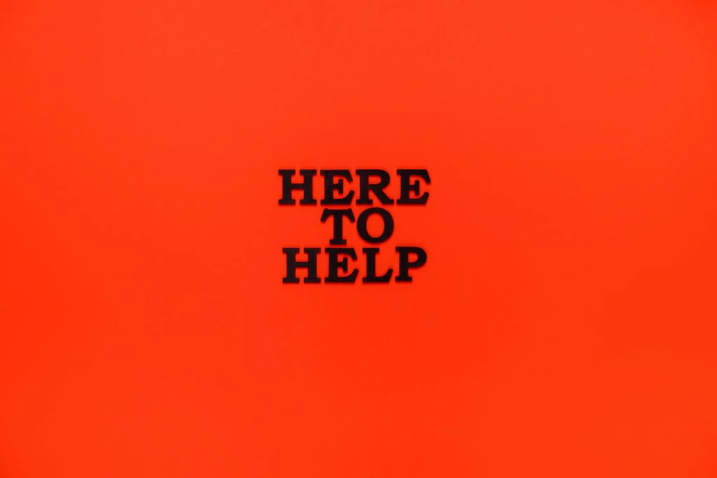 Black text reading "HERE TO HELP" is centered on a solid bright orange background.
