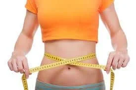 Person wearing an orange crop top measuring their waist with a yellow measuring tape.