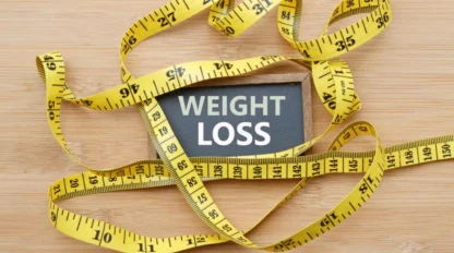 A sign reading "Weight Loss" is surrounded by a yellow measuring tape on a wooden surface.