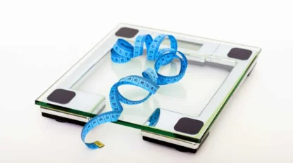 A digital glass bathroom scale with a blue measuring tape coiled on top, set against a plain white background.