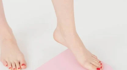A person with painted toenails steps onto a pink bathroom scale on a white floor, preparing to check their weight.