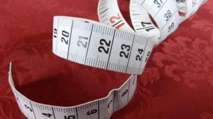 A coiled white measuring tape with black numbers is lying on a textured red surface.
