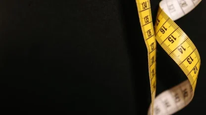 A yellow measuring tape with black numbers is hanging against a plain black background.