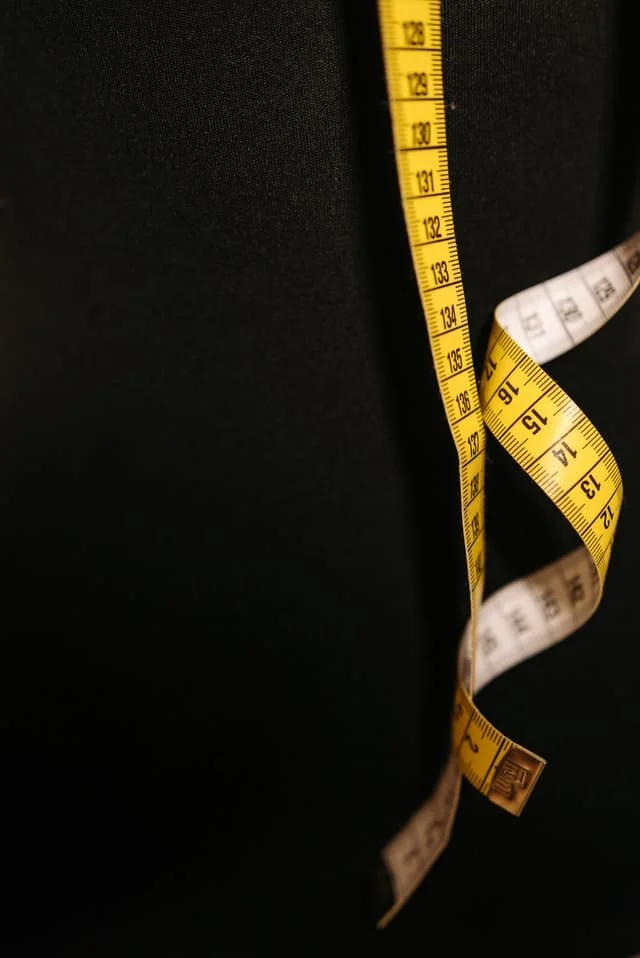 A yellow measuring tape with black numbers is hanging against a plain black background.