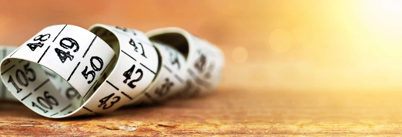 A close-up of a white measuring tape with black numbers coiled on a wooden surface, with a warm, blurred background.