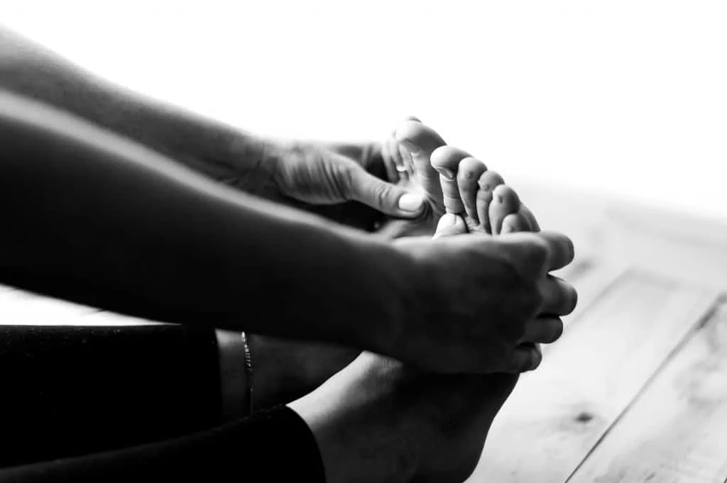 A person sits on the floor and touches their toes, stretching their legs and feet. The image is in black and white.
