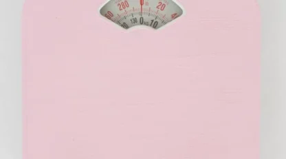 A pink analog bathroom scale with a round display showing weight measurements in kilograms and pounds, photographed from above on a white background.
