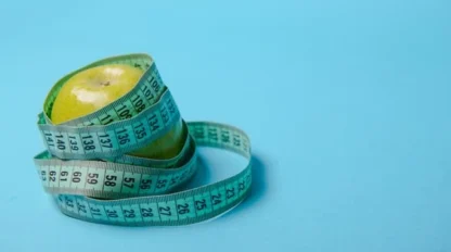 A green apple with a measuring tape wrapped around it, set against a plain blue background.