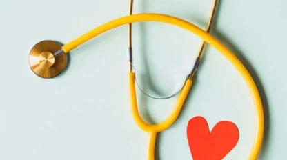 A yellow stethoscope is arranged on a light surface next to a red paper heart shape.