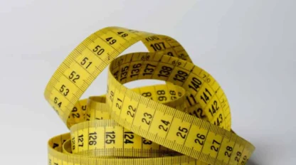 A yellow measuring tape is coiled on a white surface, displaying both metric and imperial measurement markings.