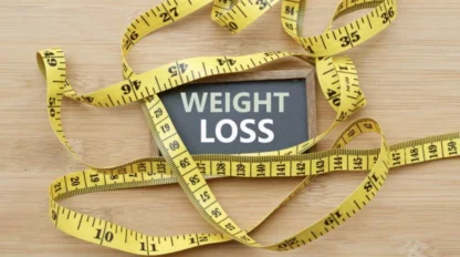 A sign reading "Weight Loss" is surrounded by a yellow measuring tape on a wooden surface.