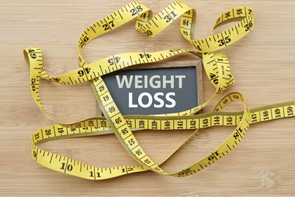 A sign reading "Weight Loss" is surrounded by a yellow measuring tape on a wooden surface.