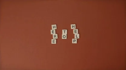 Scrabble tiles arranged on a brown background spell out the phrase "HERE TO HELP" in three vertical columns.