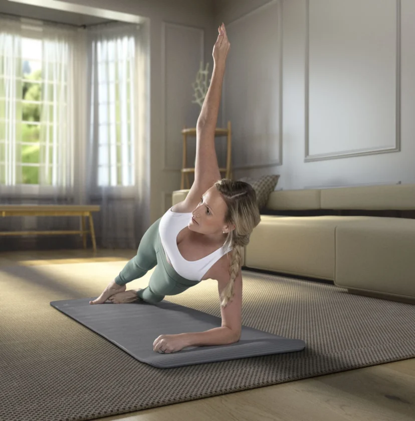 Person performing a side plank on a yoga mat in a well-lit living room with modern decor and large windows.