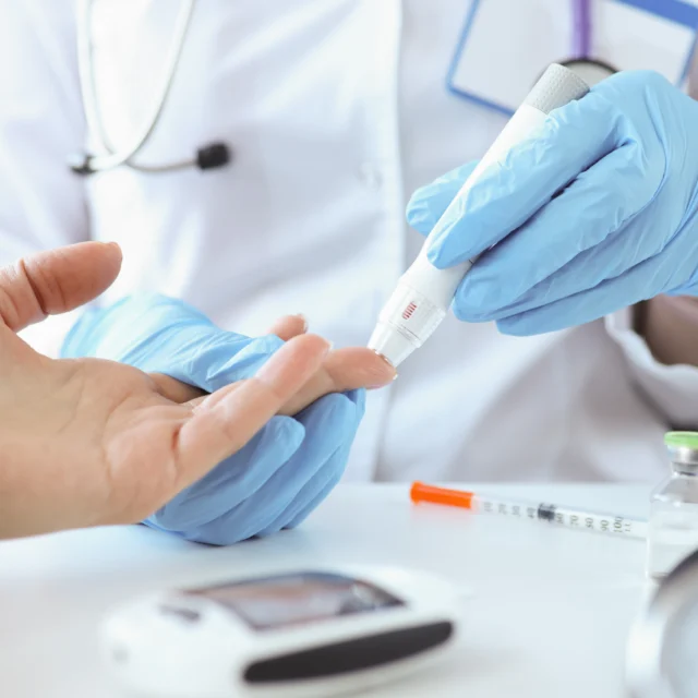 A healthcare professional wearing gloves uses a device to check a patient's blood sugar level. Medical supplies are visible on the table.