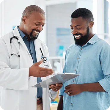A doctor in a white coat shows a clipboard to a smiling patient in a blue shirt during a consultation in a medical office.