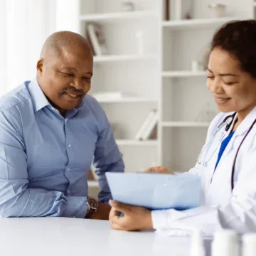 A doctor in a white coat reviews paperwork with a male patient in an office setting.