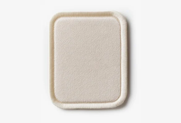 A close-up of a square, beige fabric patch with rounded corners and stitched edges on a white background.