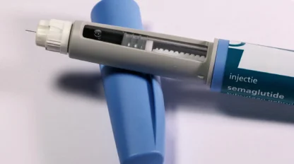 A close-up of a semaglutide injection pen with its blue cap removed, showing the needle and dosage window, placed on a white surface.