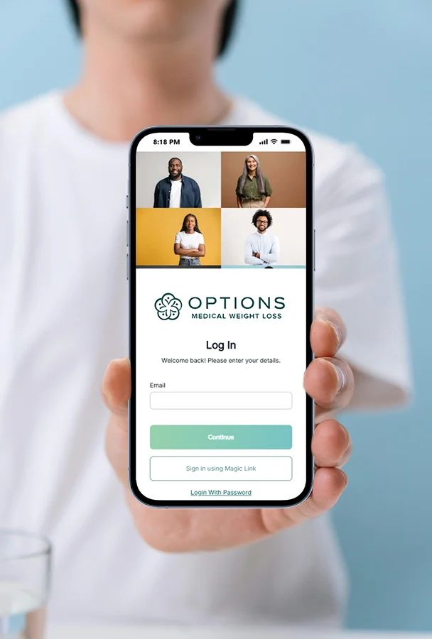 A person holds a smartphone displaying a medical weight loss app login screen, which features photos of diverse people, fields for email entry, and buttons labeled “Continue,” “Sign in using Magic Link,” and “Login With Password.”.