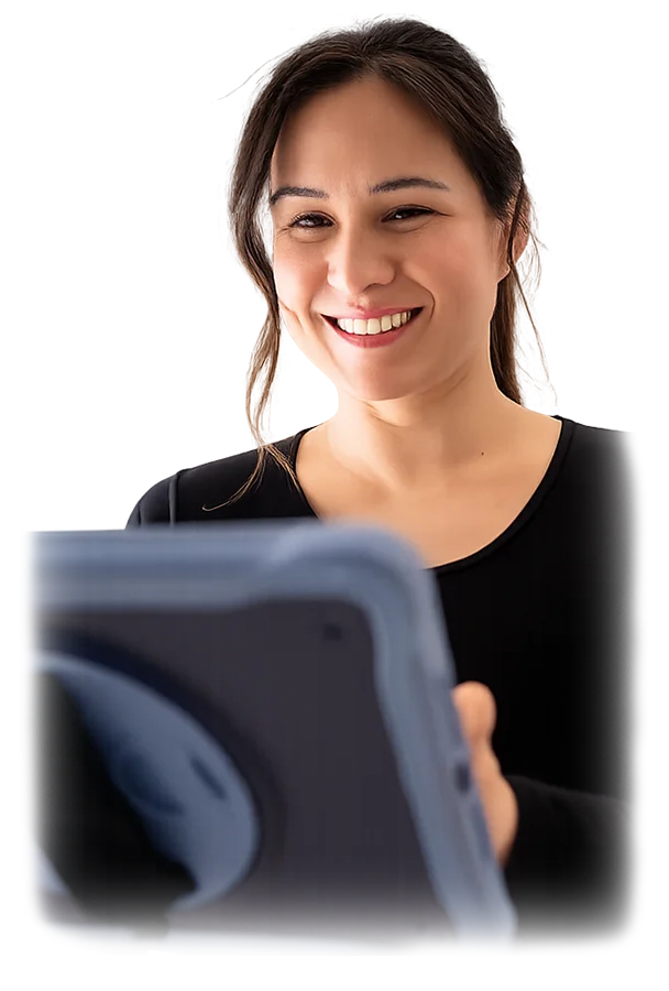 A woman with long dark hair, wearing a black top, smiles while holding and looking at a blue tablet device in front of her. The background is blurred.